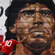 A boy touches a mural of Diego Maradona outside the stadium of Argentinos Juniors, where he started as a professional