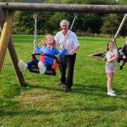 Councillor Steve Kay with (left to right) grandchildren Emily, Penelope and Thomas on the playing field at Charltons after swings were refurbished