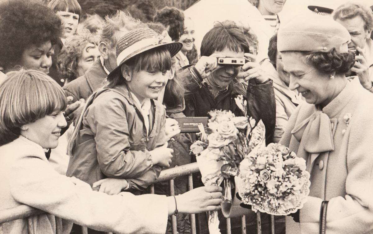 The moment the Queen receives a posy is captured on an instamatic camera with a fold-out handle