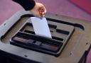 A person places a ballot paper into a ballot box