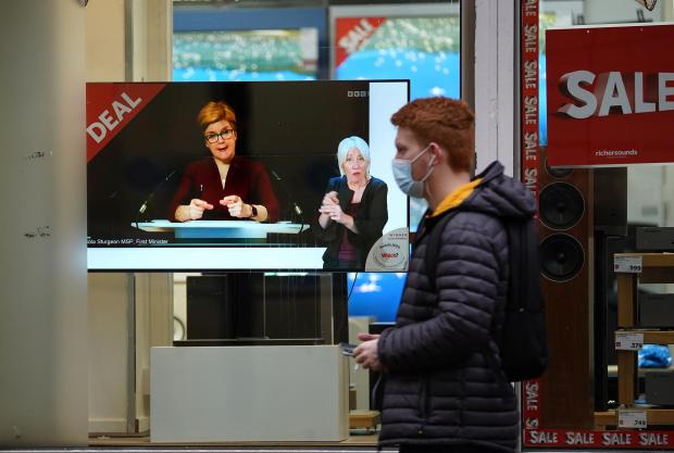 The Northern Echo: Passers-by look at a tv screen in a Glasgow shop showing First Minister Nicola Sturgeon making a Covid-19 statement during a virtual sitting of the Scottish Parliament. Photo taken on December 29, 2021, via PA.