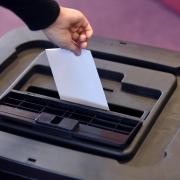 A person places a ballot paper into a ballot box