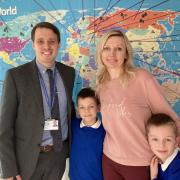 Headteacher Mark Dipple with Ukrainian mum, Maria Vasylyshyn, and her sons, Ostap and Artem, in front of the map showing the pupils' countries