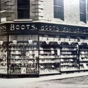 FIRST GLANCE: The original Boots shop front with Victoria Avenue going off to the right and Newgate Street to the left. A poster in the window advertises “Pure Drugs” – a Victorian Boots tradename. Above the window on the left are two enamel signs.
