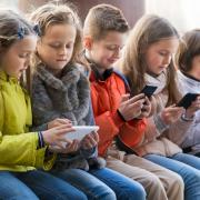 Ordinary kids sitting with mobile devices in street