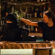 Alone in the bistro, Kate Connor [FAYE BROOKES] and Rana Nazir [BHAVNA LIMBACHIA] kiss passionately. Having heard a noise in the kitchen, Kate and Rana hide under a table. They watch as a dark figure appears and empties the till. As the thief makes to