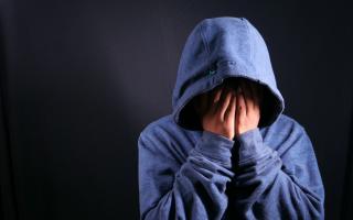 A person wearing a blue hoodie with their hands over their face. Credit: Canva
